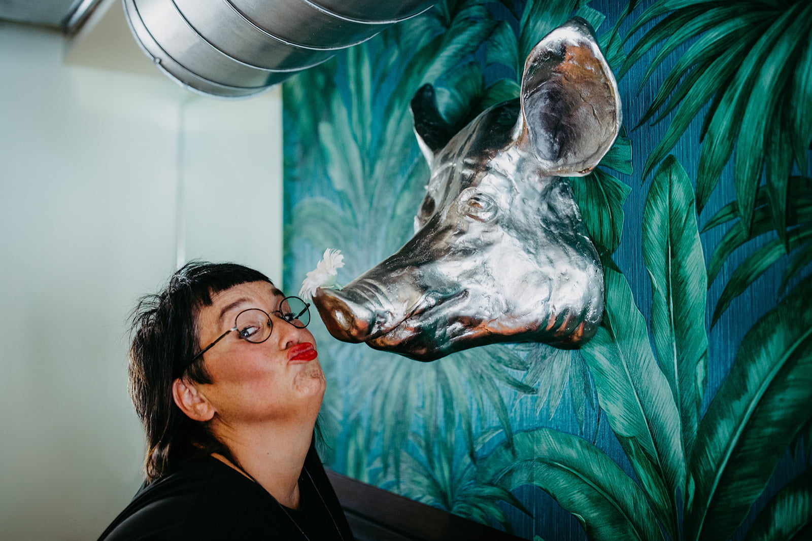 Glück! Sabine küsst die Skulptur eines silbernen Wildschweins an einer Wand
